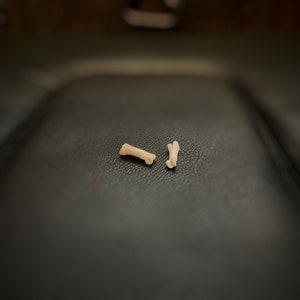 Può includere: Due piccoli frammenti di osso marrone chiaro su una superficie in pelle grigia scura.