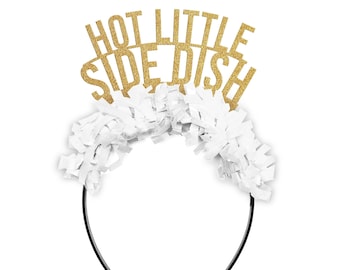 May include: A festive headband with the text "HOT LITTLE SIDE DISH" in gold glitter letters. The headband features a white fringe and a black plastic band, perfect for parties and celebrations.
