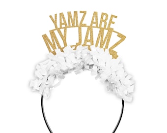 May include: A festive headband with the text "YAMZ ARE MY JAMZ" in gold glitter. The headband features white paper fringe and a black plastic band, perfect for a party or celebration.