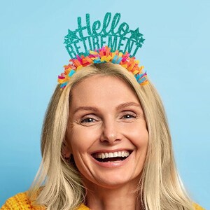 May include: A woman wearing a yellow sweater smiles while wearing a teal blue headband with the text "Hello Retirement" and colorful streamers.