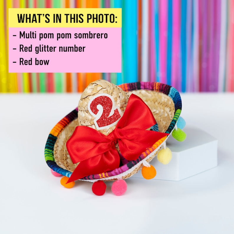 Op de afbeelding: Een kleine, veelkleurige pompon sombrero met een rood glitter nummer "2" en een rode strik.