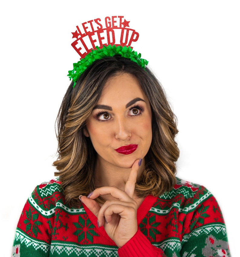 Puede incluir: Una mujer con un jersey navide&ntilde;o rojo, verde y blanco y una diadema que dice "LET'S GET ELFED UP". La diadema tiene una base de volantes verdes y texto con purpurina roja. La mujer mira hacia arriba y a la derecha, con el dedo en la barbilla.