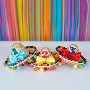 Op de afbeelding: Drie kleurrijke mini-sombreros met pompoenen, elk versierd met een nummer, een strik en glitter. De sombreros zijn genummerd 1, 2 en 3.