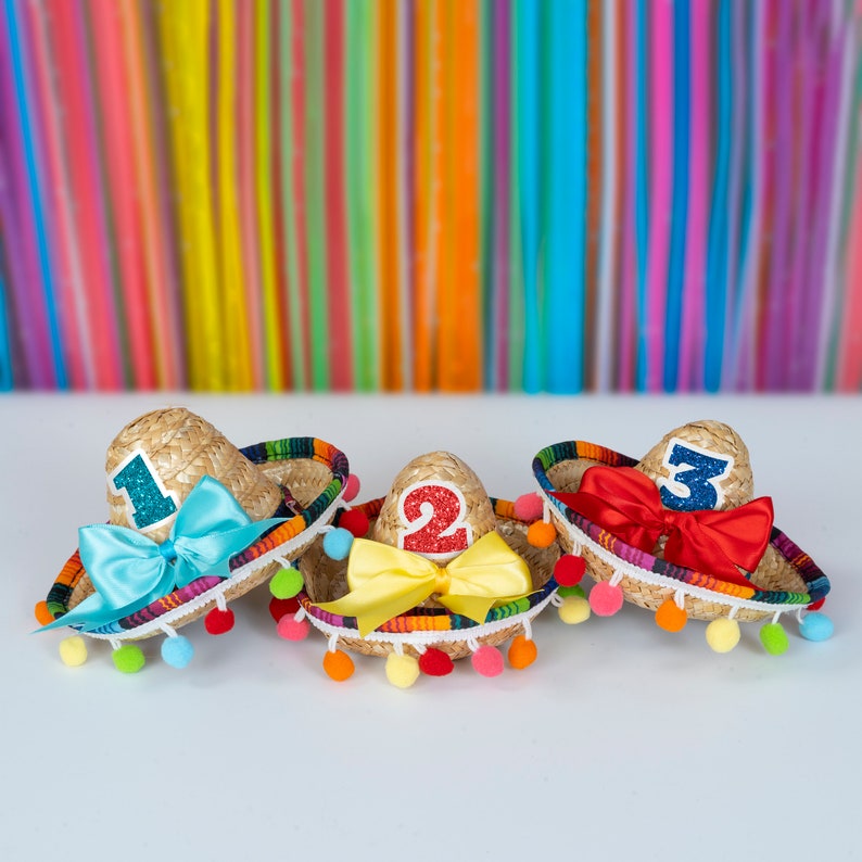 Op de afbeelding: Drie kleurrijke mini-sombreros met pompoenen, elk versierd met een nummer, een strik en glitter. De sombreros zijn genummerd 1, 2 en 3.