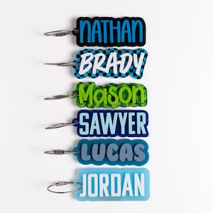 May include: Six rectangular personalized luggage tags with rounded edges, each featuring a unique name: NATHAN, BRADY, Mason, SAWYER, LUCAS, and JORDAN. Each tag includes a silver-toned metal wire loop for attachment and displays distinct color schemes.