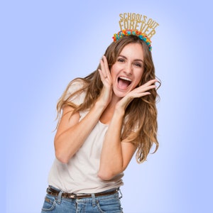 May include: A woman wearing a white t-shirt and blue jeans is smiling and holding her hands to her face. She is wearing a gold glitter headband that says "Schools Out Forever".