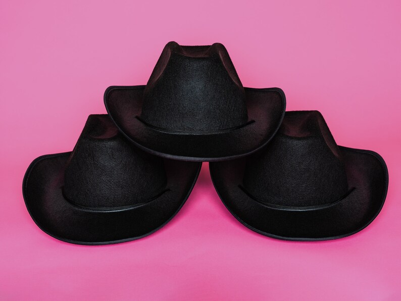 K&ouml;nnte beinhalten: Drei schwarze Cowboyh&uuml;te, die &uuml;bereinander auf einem rosa Hintergrund gestapelt sind.