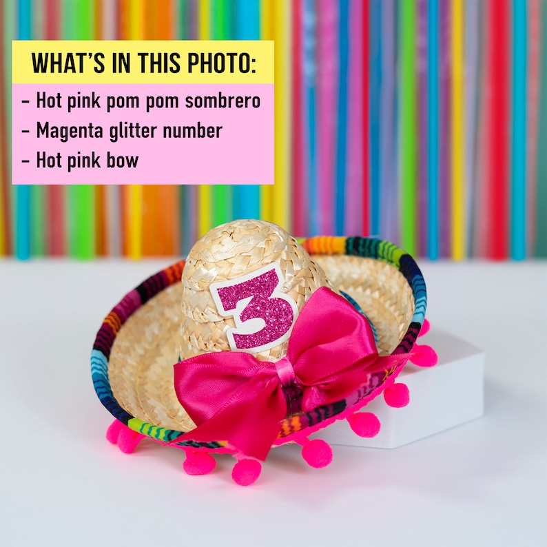 Op de afbeelding: Een kleine strooien sombrero met een roze pompon rand en een roze strik. De sombrero heeft een magenta glitter nummer "3" aan de voorkant.