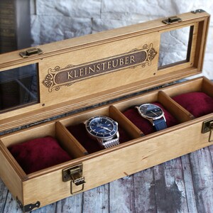 May include: A wooden watch box with a glass top and a velvet interior. The box has a personalized inscription that reads "KLEINSTEUBER".