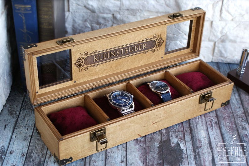May include: A wooden watch box with a glass top and a velvet interior. The box has a personalized inscription that reads "KLEINSTEUBER".