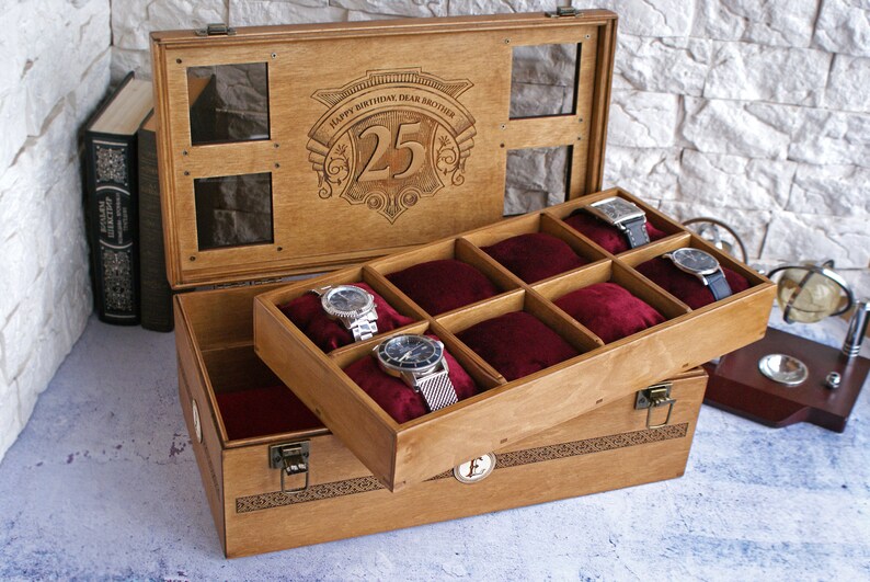 May include: A wooden watch box with a hinged lid and a velvet interior. The lid has a clear glass window and is engraved with the text "Happy Birthday Dear Brother 25". The box has eight compartments for storing watches.