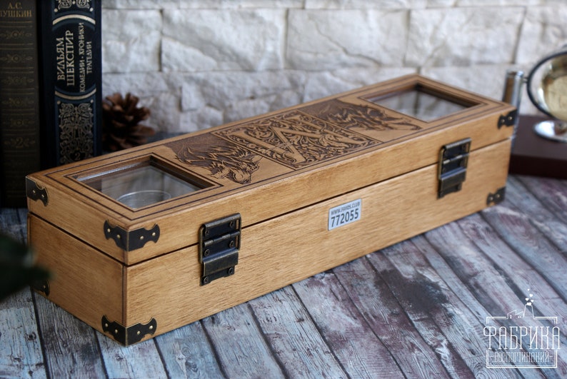 May include: A wooden box with a hinged lid and brass accents. The box has a glass window on the top and is engraved with a design of a wolf and the letter "W". The box has a label on the bottom with the number "772055".
