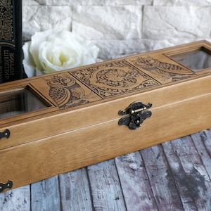 May include: A wooden box with a hinged lid and a brass latch. The box is decorated with an engraved design of owls and floral patterns. The box has two glass windows on the top.