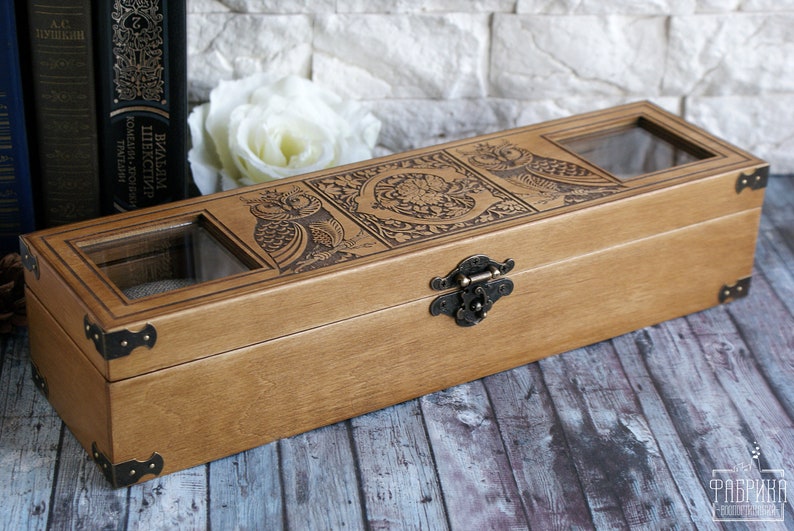 May include: A wooden box with a hinged lid and a brass latch. The box is decorated with an engraved design of owls and floral patterns. The box has two glass windows on the top.