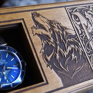 May include: A wooden watch box with a blue watch inside. The box is engraved with a wolf and the letter "M" in a decorative font. The text "Фабрика - воплощения" is also engraved on the box.