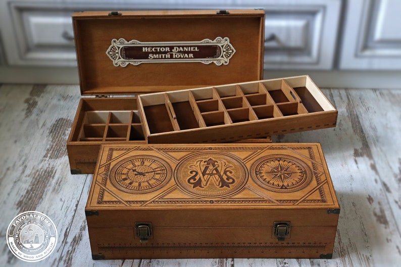 May include: A wooden box with a hinged lid and a compartment for storing small items. The box is decorated with an engraved design featuring a clock, compass, and initials. The lid has a label with the name "Hector Daniel Smith Jovan".
