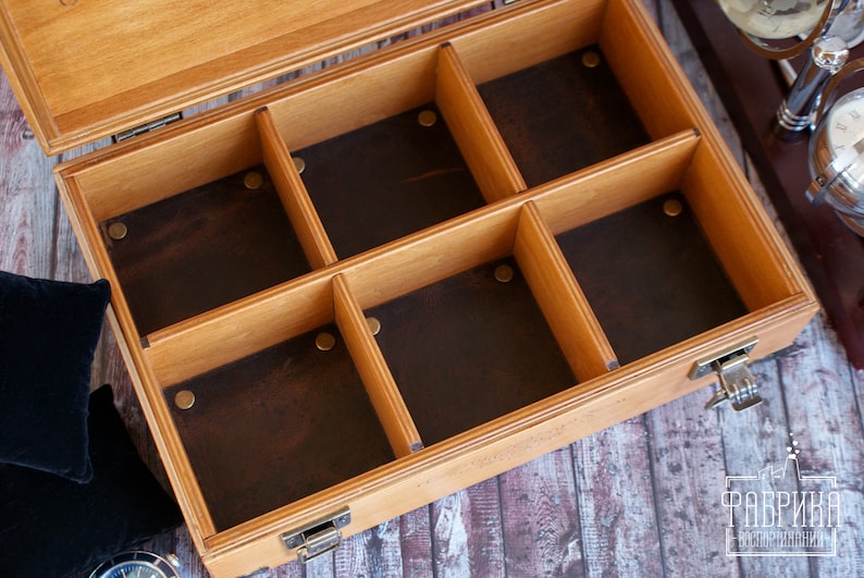 K&ouml;nnte beinhalten: Offene Holzkiste mit sechs F&auml;chern, die mit braunem Filz ausgekleidet sind. Die Kiste hat einen Messingverschluss an der Seite.