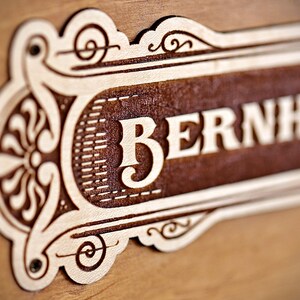 May include: A wooden sign with an ornate design and the name "BERNHARD" carved into it.