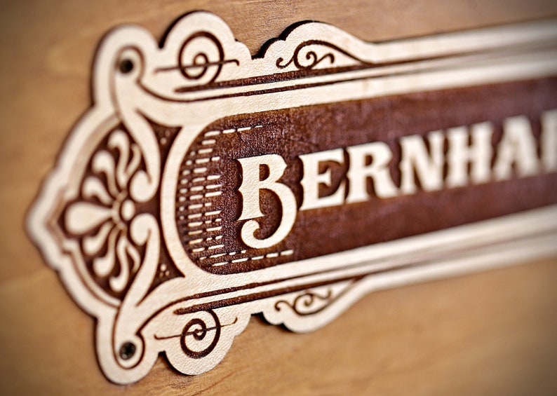 May include: A wooden sign with an ornate design and the name "BERNHARD" carved into it.