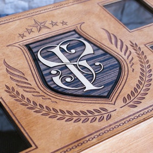 Puede incluir: Una caja de madera con un dise&ntilde;o decorativo que presenta un escudo con las iniciales "SF" y una corona de laurel. La caja tiene cinco estrellas y varias ventanas de vidrio.