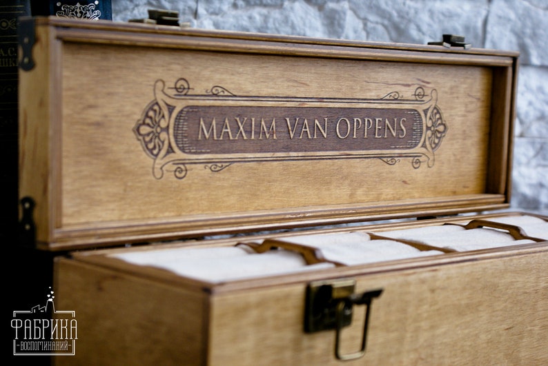 May include: A wooden box with a hinged lid and a decorative engraved inscription that reads "MAXIM VAN OPPENS". The box has a latch and is divided into compartments.