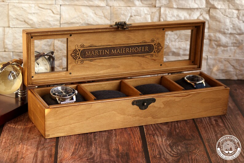 May include: A wooden watch box with a clear glass top and four compartments. The box is engraved with the name "MARTIN MAIERHOFER".