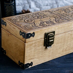 May include: A wooden box with a carved design of a lion and floral patterns. The box has a brass latch and metal corner accents.