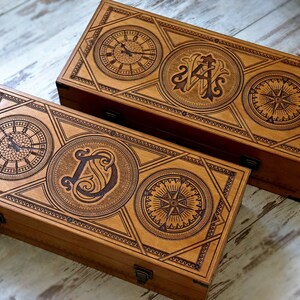 May include: Two wooden boxes with intricate designs. The top box features a compass, a clock, and the initials "A.S." The bottom box features a compass, a clock, and the initial "D".