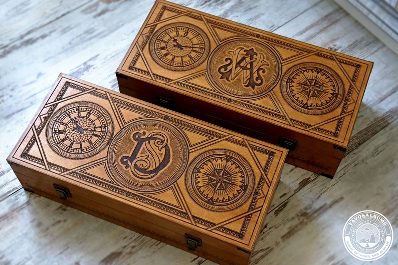 May include: Two wooden boxes with intricate designs. The top box features a compass, a clock, and the initials "A.S." The bottom box features a compass, a clock, and the initial "D".