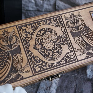May include: A wooden box with a hinged lid, featuring intricate laser-engraved designs of owls and floral patterns. The box has a brass latch and a clear glass window.