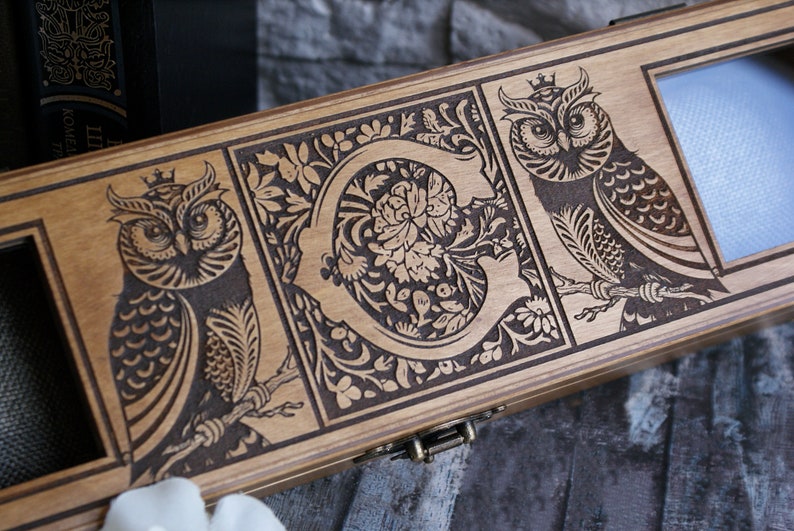 May include: A wooden box with a hinged lid, featuring intricate laser-engraved designs of owls and floral patterns. The box has a brass latch and a clear glass window.