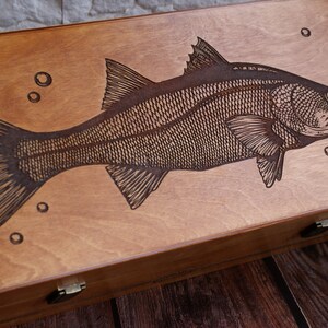 K&ouml;nnte beinhalten: Eine Holzkiste mit einem lasergravierten Bild eines Fisches. Der Fisch ist detailliert mit Schuppen und Flossen dargestellt. Die Kiste ist braun gebeizt und hat zwei Messing Scharniere.