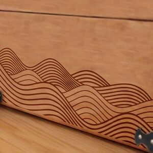 May include: A wooden box with a decorative wave pattern carved into the front. The box has metal corner accents.
