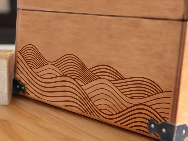 May include: A wooden box with a decorative wave pattern carved into the front. The box has metal corner accents.