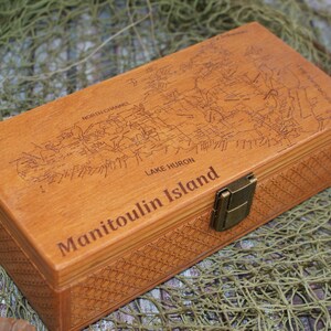 Op de afbeelding: Een houten doos met een gegraveerde kaart van Manitoulin Island, Lake Huron, op de deksel. De doos heeft een messing sluiting en een geweven patroon aan de zijkanten.