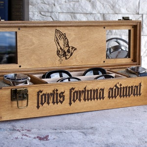 Peut inclure: Une bo&icirc;te de rangement rectangulaire en bois avec un couvercle &agrave; charni&egrave;re dot&eacute; de deux fen&ecirc;tres en verre et d'une gravure de mains en pri&egrave;re. L'avant de la bo&icirc;te pr&eacute;sente le texte latin grav&eacute; fortis fortuna adiuvat et deux loquets en m&eacute;tal.