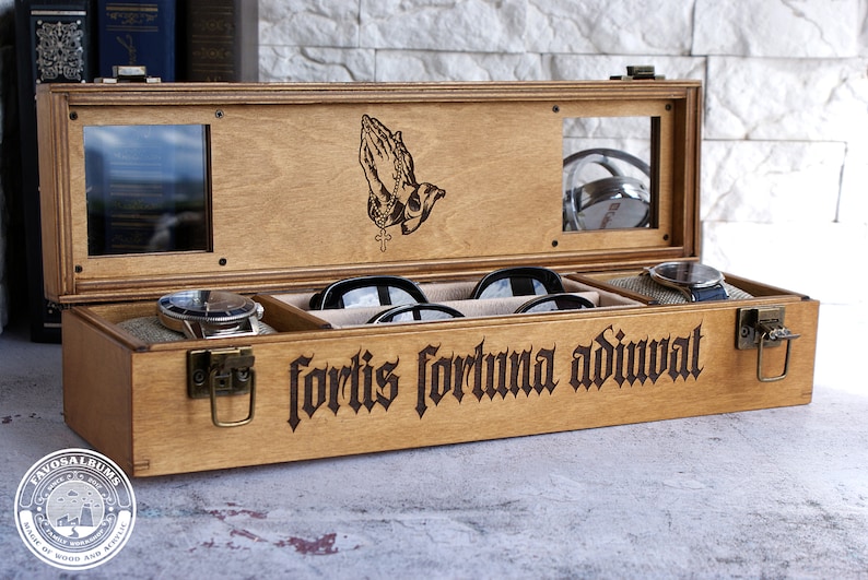 Peut inclure: Une bo&icirc;te de rangement rectangulaire en bois avec un couvercle &agrave; charni&egrave;re dot&eacute; de deux fen&ecirc;tres en verre et d'une gravure de mains en pri&egrave;re. L'avant de la bo&icirc;te pr&eacute;sente le texte latin grav&eacute; fortis fortuna adiuvat et deux loquets en m&eacute;tal.