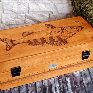 May include: A wooden box with a fish design engraved on the lid. The box has a ruler on the side and a metal latch. The box is labelled "Фабрика воспоминаний" which translates to "Factory of Memories".