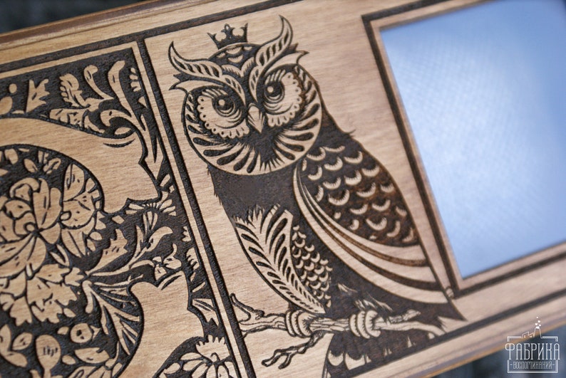 May include: A wooden picture frame with a decorative design of a crowned owl and floral patterns. The frame has a blank space for a photo.