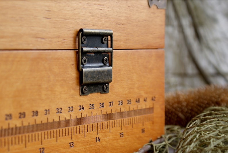 May include: A wooden box with a brass hinge and a ruler printed on the front. The ruler is marked with numbers from 28 to 42.