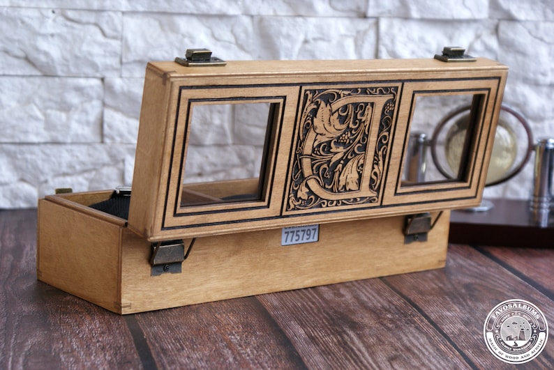 K&ouml;nnte beinhalten: Eine Holzkiste mit einem Scharnierdeckel, die drei F&auml;cher mit Glasfenstern bietet. Das mittlere Fach hat ein filigranes Blumenmuster mit dem eingravierten Buchstaben "D". Die Kiste hat einen Messingverschluss und die Nummer "775797" ist auf der Unterseite aufgedruckt.