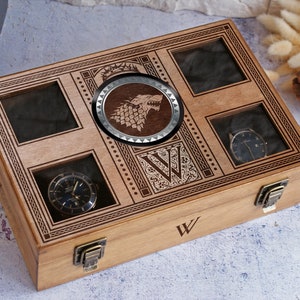 May include: A wooden watch box with a glass top and a wolf emblem. The box has a compartment for five watches and is engraved with the letter "W".