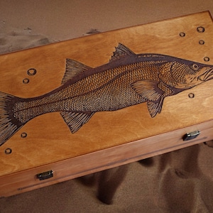 K&ouml;nnte beinhalten: Eine Holzkiste mit einem Scharnierdeckel, auf dem ein Laser-graviertes Bild eines Fisches mit Blasen zu sehen ist. Die Kiste hat zwei Messing-Scharniere und einen Messing-Verschluss.