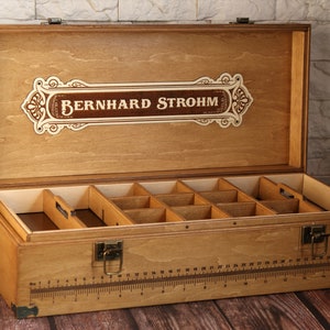 May include: A wooden box with a hinged lid and a label that reads "Bernhard Strohm". The box has a ruler on the front and is divided into compartments inside.