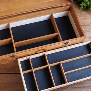 May include: A wooden box with a hinged lid and two compartments. The top compartment has a black felt lining and is divided into several sections. The bottom compartment has a black felt lining and is divided into smaller sections.
