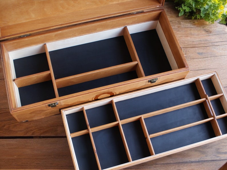 May include: A wooden box with a hinged lid and two compartments. The top compartment has a black felt lining and is divided into several sections. The bottom compartment has a black felt lining and is divided into smaller sections.
