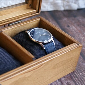 May include: A wooden watch box with a blue velvet interior. A silver watch with a blue face and a blue leather band is resting in the box.