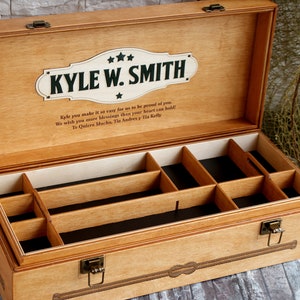 May include: A wooden box with a personalised inscription for "Kyle W. Smith". The box has a hinged lid and a compartment with multiple dividers. The inscription reads "Kyle you make it so easy for us to be proud of you. We wish you more blessings than your heart can hold. Te Quiero Mucho, Tia Andrea y Tia Kelly."