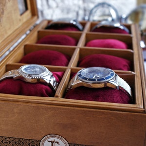 May include: A wooden watch box with a hinged lid, lined with red velvet, and containing two silver watches with blue faces.
