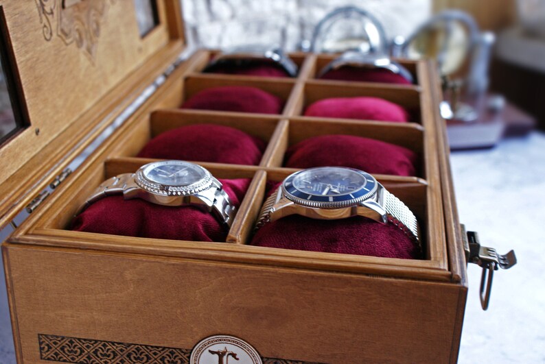 May include: A wooden watch box with a hinged lid, lined with red velvet, and containing two silver watches with blue faces.